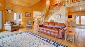 A spacious log cabin interior with a leather sofa, a patterned rug, and a staircase leading to an upper level. - A True Montana Cabin with Sweeping Views of the Mountains and the Madison River. (Cameron)