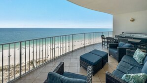 A balcony with a view of the beach and ocean, furnished with wicker sofas and a table.