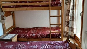 Ein Schlafraum mit Etagenbetten, einer gemusterten Bettdecke, einer Holzleiter und einem fenster mit Vorhängen.