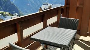 Ein Balkon mit zwei Korbstühlen und einem Tisch, mit Blick auf eine gebirgige Landschaft und Gebäude im Hintergrund.