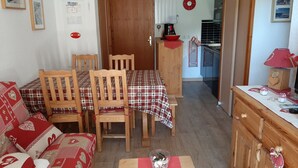 Ein gemütlicher Essbereich mit Holztisch und -stühlen, im Hintergrund ist eine Küche erkennbar, und ein rot-weiß karierter Tischläufer.