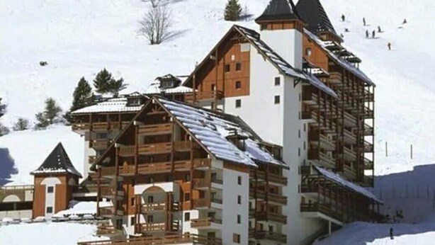 Ein mehrstöckiges Holzgebäude mit Balkonen, umgeben von verschneiter Landschaft und Skipisten.