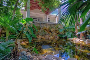 Un jardín tranquilo con un estanque, abundante vegetación y un muro de piedra.