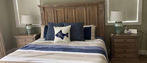 Une chambre à coucher avec une tête de lit en bois, un lit avec une literie bleue et blanche, deux tables de chevet avec des lampes et un panneau décoratif mural.