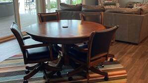 Un coin repas avec une table ronde et des chaises, un tapis rayé aux couleurs vives, et une vue sur une terrasse avec des chaises et une table.