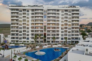 A modern hotel with a central swimming pool, multiple balconies, and a landscaped outdoor area.