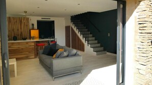 A modern living room with a grey sofa, a wooden dining area, and a staircase leading to an upper floor.