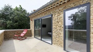 A modern outdoor patio with stone walls, a red rocking chair, and large sliding glass doors.