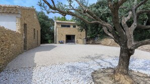 A rustic stone building with a gravel driveway and a large tree in the foreground.