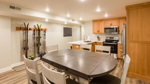 A modern kitchen with wooden cabinets, a microwave, an oven, and a refrigerator. There is a dining table with chairs and a ski rack against the wall. - Gorgeous brand new 2BR unit, sleeps 6.  Amazing ski location! (Salt Lake City)