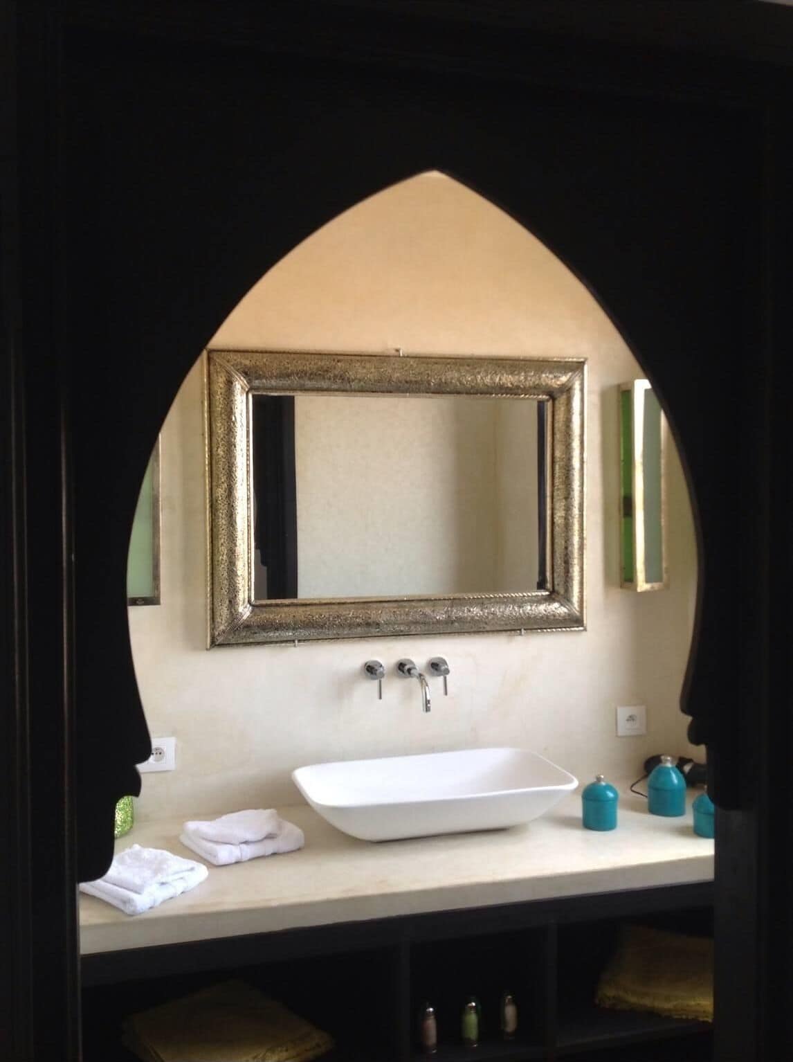A bathroom with a white sink, two faucets, and a large mirror framed in gold.
