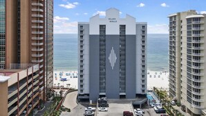 A high-rise hotel with a central entrance, a beach view, and a parking area.
