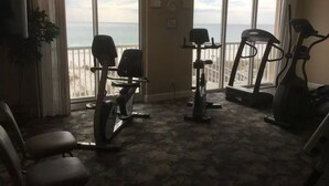 A fitness room with exercise equipment, large windows, and a view of the ocean.