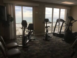 Uma sala de ginástica com equipamentos de exercício, janelas amplas e vista para o mar.