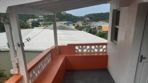 Ein Balkon mit Betonboden, weißen und orangefarbenen Wänden und Blick auf Gebäude im Hintergrund.