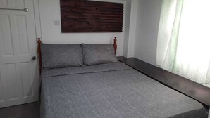 Ein Schlafzimmer mit einem Bett, einem Holz-Kopfteil, einem Fenster mit Vorhängen und einer weißen Tür.
