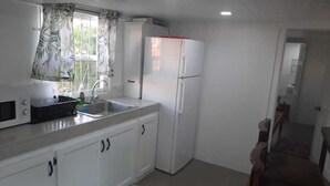 Eine kleine Küche mit weißen Schränken, einer Mikrowelle, einem Spülbecken und einem weißen Kühlschrank.