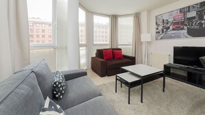 A modern living room with a grey sofa, a brown sofa with red cushions, a black TV stand, and a painting of a red double-decker bus. - Apartment (Madrid)