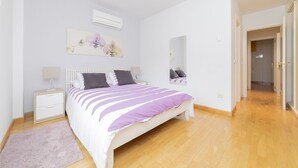 A bedroom with a bed, nightstands, a mirror, and a door leading to another room. - Apartment (Madrid)