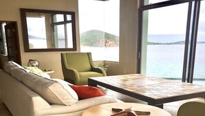 A modern living room with a sofa, a round wooden table, and a view of the sea through large windows. - Winter Waterfront, amazing views of the Caribbean Seas. (St Thomas)