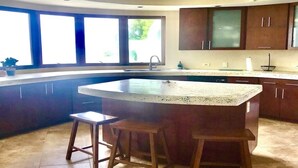 A kitchen with a curved island, two stools, a ceiling fan, and large windows. - Winter Waterfront, amazing views of the Caribbean Seas. (St Thomas)
