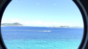 A view through a round window of a body of water with a distant landmass and a boat. - Winter Waterfront, amazing views of the Caribbean Seas. (St Thomas)
