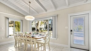 A dining area with a wooden table and chairs, large windows, and a door with a security screen. - Sandy Rocks | Ultimate Bundle: 2 Private Pet Friendly Homes, 2 Private Heated Pools, Walk to Beach! (Siesta Key)