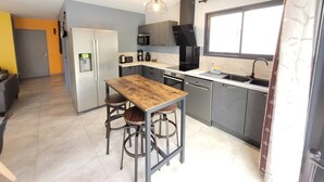 A compact kitchen with a refrigerator, microwave, stove, sink, and a wooden table with stools. - Magnificent South-facing Villa with Jaccuzzi, Beach and Corniche 200 m'away (Saint-Hilaire-de-Riez)