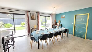 A dining area with a table set for six, chairs, a hanging light fixture, and a view of the outdoors. - Magnificent South-facing Villa with Jaccuzzi, Beach and Corniche 200 m'away (Saint-Hilaire-de-Riez)