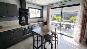 A modern kitchen with dark cabinetry, a wooden bar counter, and a view of the outdoor patio area. - Magnificent South-facing Villa with Jaccuzzi, Beach and Corniche 200 m'away (Saint-Hilaire-de-Riez)