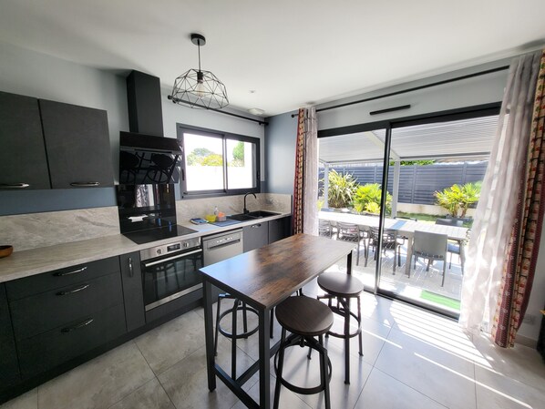 A modern kitchen with dark cabinetry, a wooden bar counter, and a view of the outdoor patio area.