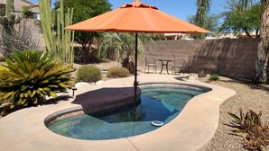 A swimming pool with a curved edge, surrounded by a patio area with a brick wall, a table with chairs, and various plants including a large cactus. - CASA GRIS-Heated spool-Bring your fur baby! Enjoy Naranja Park and bike trails. (Tucson)