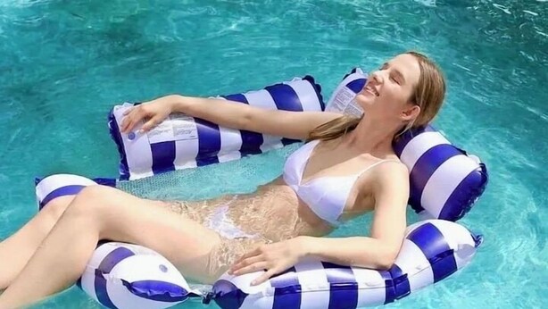 Une personne allongée sur un flotteur bleu et blanc à rayures, dans une piscine à l’eau d’un bleu limpide.