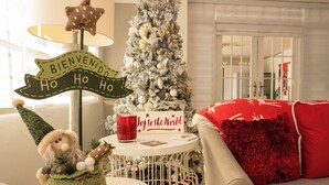 Une pièce décorée sur le thème de Noël, avec un sapin de Noël blanc, une petite table sur laquelle est posé un panneau indiquant « Joie au monde », un Père Noël tricoté vert et une bougie rouge.