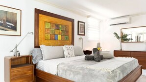 Une chambre à coucher avec un lit en bois, une table de chevet, une commode, un miroir et des œuvres d’art accrochées au mur.