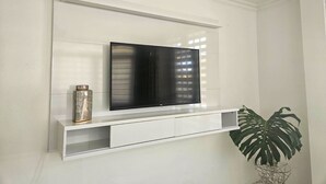 Un televisor blanco montado en la pared, con un estante debajo.
