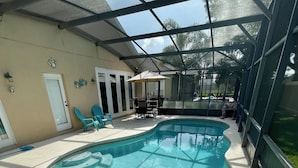 A swimming pool with a glass enclosure, a patio area with chairs and a table, and a door with a window. - Davenport Disney-Area Home ~ Private Pool & Hot Tub ~ Quiet Retreat (Davenport)