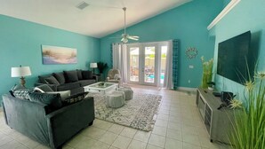 A living room with a sofa, coffee table, and a TV. There is a door leading to a balcony with outdoor furniture. - Davenport Disney-Area Home ~ Private Pool & Hot Tub ~ Quiet Retreat (Davenport)