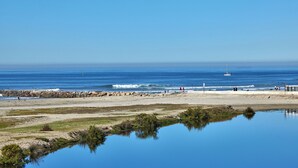 A beach with a calm sea, a sailboat, and a rocky shoreline. - Panoramic Ocean, Marina & River Views - Steps to Beach & Harbor (Oceanside)