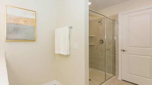 A bathroom with a glass shower enclosure, a white door, and a framed abstract painting on the wall. - Elegant Apartment 3BR/2BA • Near Disney • Storey Lake Resort [SL47318] (Kissimmee)
