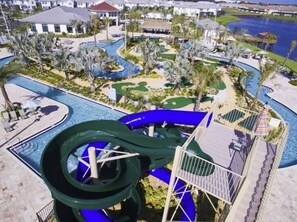 Een waterpark met een lange groene glijbaan, palmbomen en een zwembad.