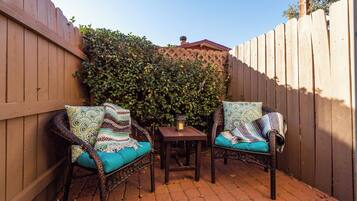 Une terrasse avec deux fauteuils en osier dotés de coussins à motifs, une petite table sur laquelle est posée une lanterne, et une clôture en bois.