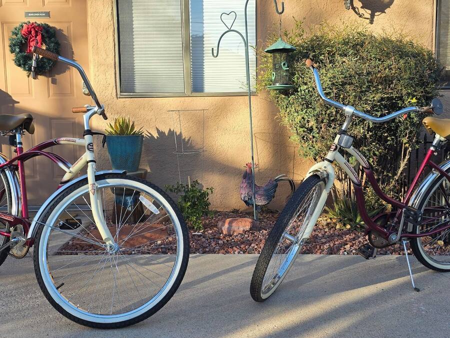 Dos bicicletas estacionadas frente a una casa con un adorno floral en la puerta, una planta en maceta y un comedero para pájaros.