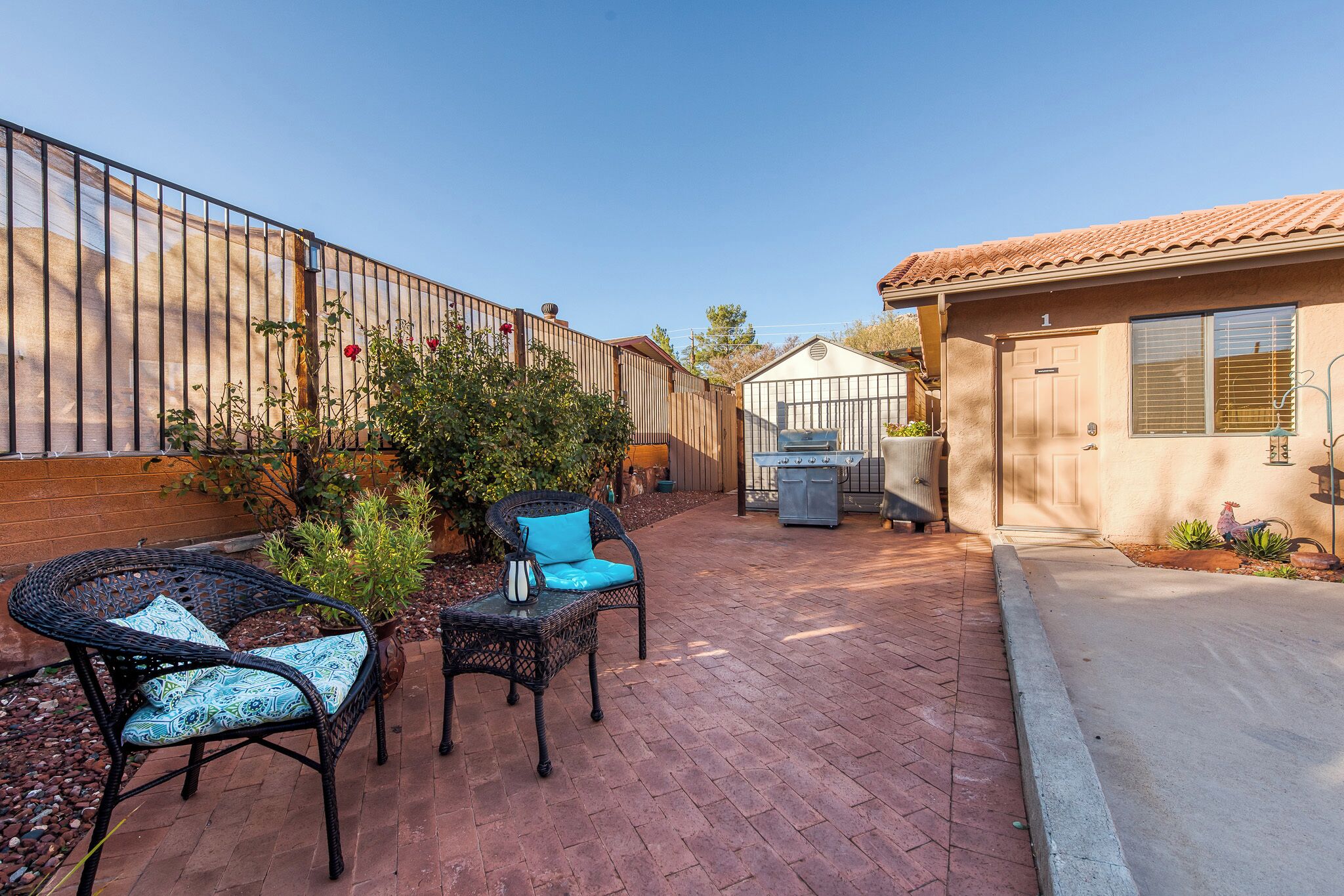 Un patio con mobiliario de mimbre, un cobertizo pequeño y una casa con techo de tejas.