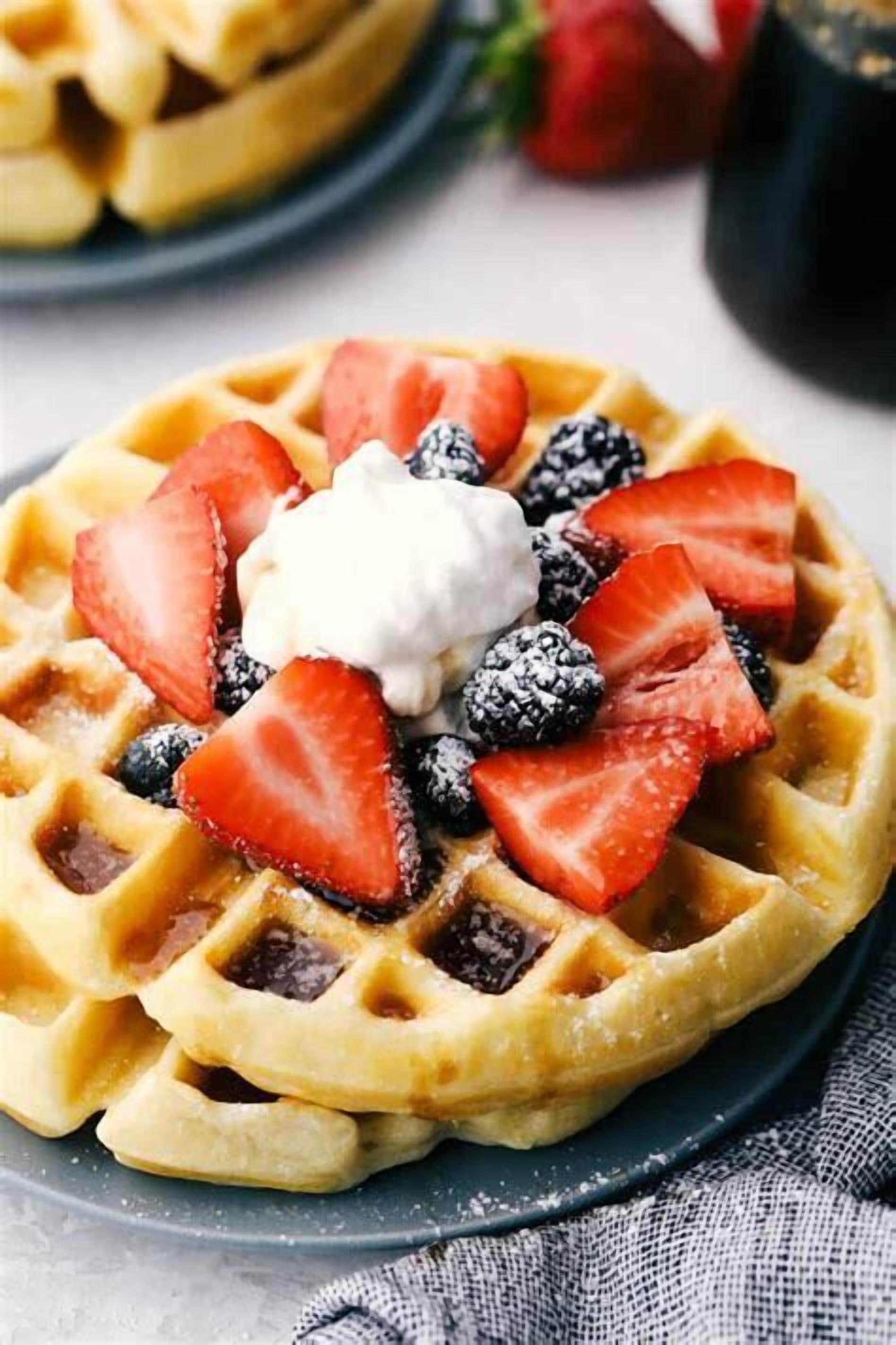 A close-up of a Belgian waffle topped with strawberries, blueberries, blackberries, and whipped cream.