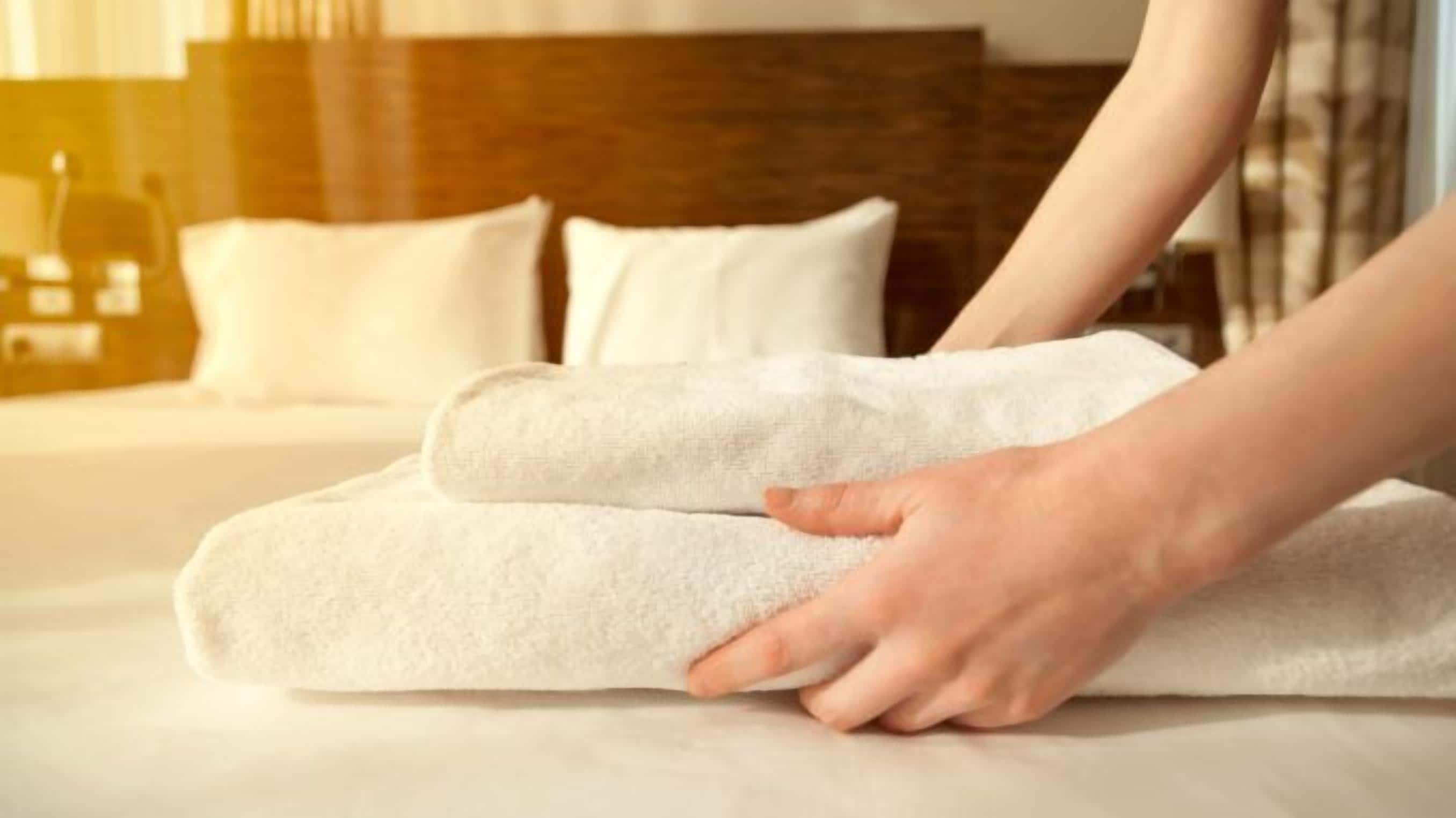 Une serviette soigneusement pliée est posée sur un lit doté d’une tête de lit en bois et de coussins blancs.