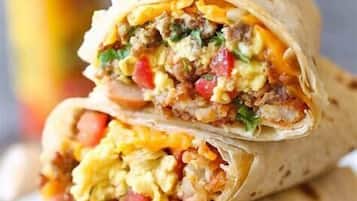 Un burrito cortado por la mitad, mostrando su relleno de huevos revueltos, carne y vegetales.