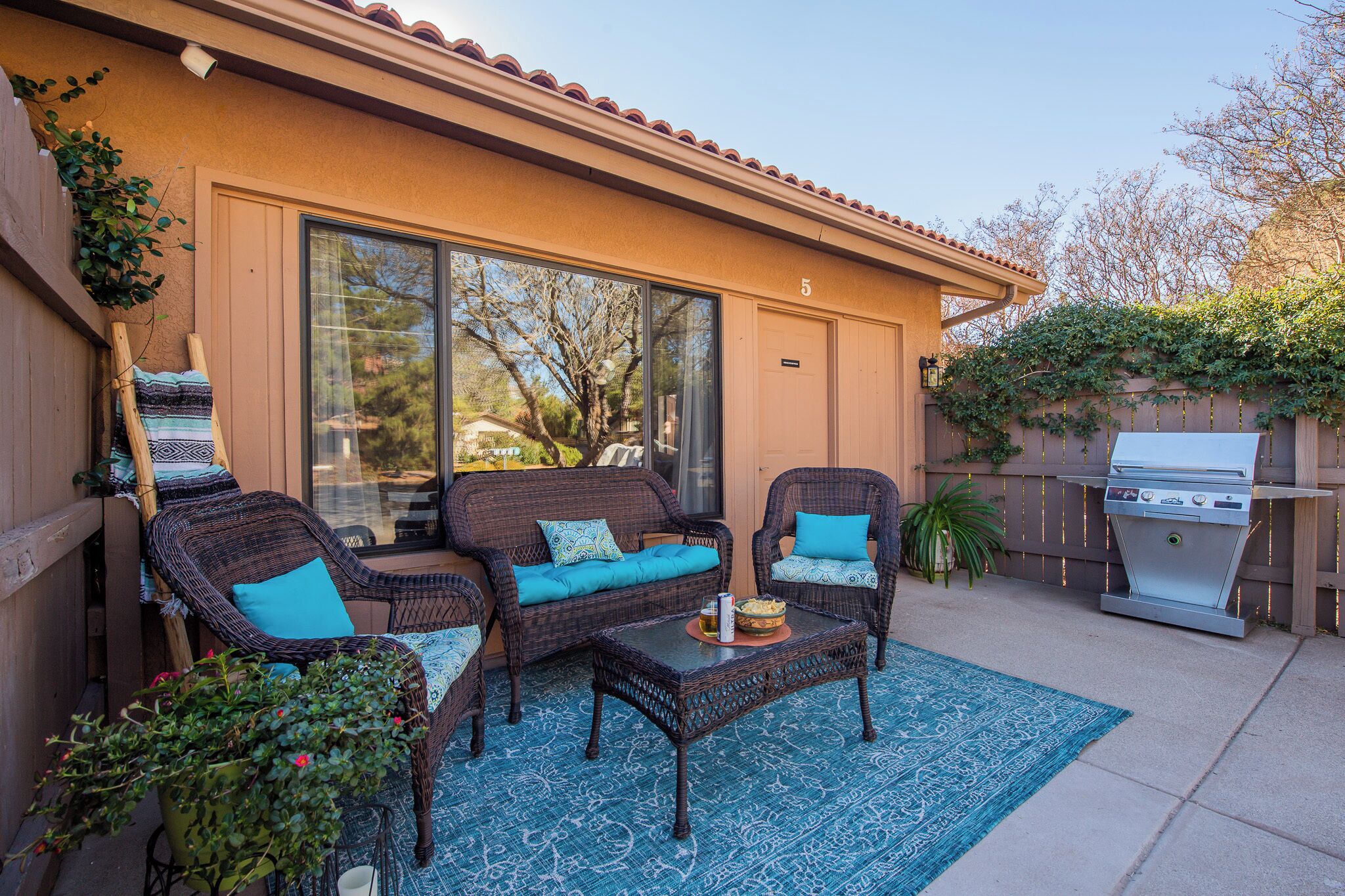 A patio with wicker furniture, a grill, and a potted plant.