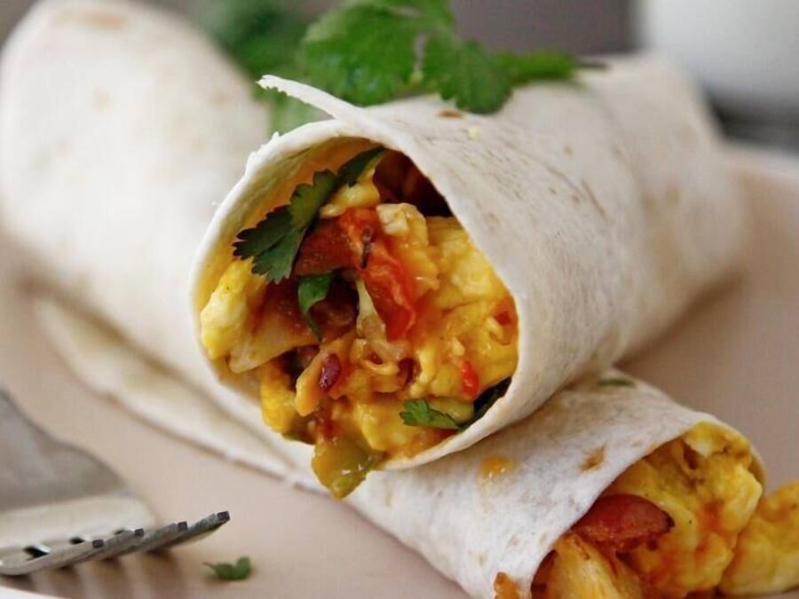 Un burrito servi sur une assiette, avec une fourchette à côté.