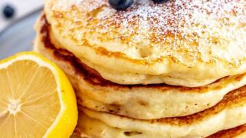 A stack of pancakes with blueberries and lemon slices on a plate.